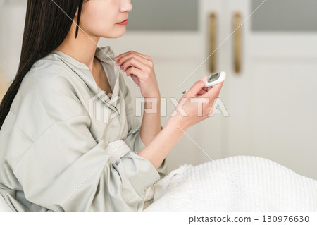 Unwell Japanese woman measuring her temperature in bed (fever, basal body temperature) 130976630