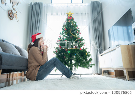 Catholic woman praying to god after decorated a Christmas tree during Christmas festival. By raising hands in prayer, the worshipper approaches the realm of the heavenly gods. 130976805