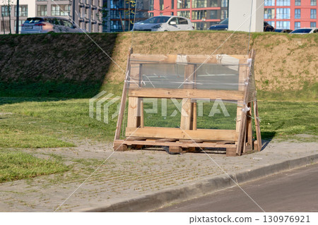 A wooden frame, covered in transparent plastic, stands amidst a vibrant urban landscape 130976921