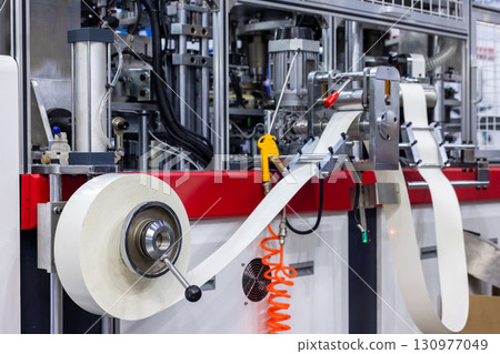 Paper drink cup making machine, Paper cup machine engaged in industrial production, Paper cup on automatic manufacturing process in factory. Paper drink cup making machine, Paper cup machine engaged in industrial production, Paper cup on automatic manufacturing process in factory. 130977049