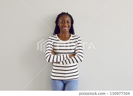 Portrait of happy young African American woman in casual clothes standing by wall 130977304