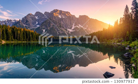 A tranquil mountain lake at sunrise reflects the scenic forest and sky, with a majestic view of the autumn peaks 130977917