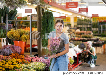 Young woman customer choosing bundle of limonium in open-air plants market 130978051