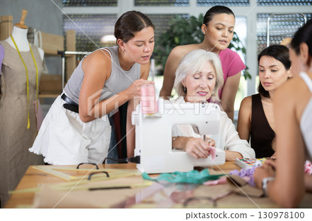 Elderly female teacher shows group how to sew Elderly female teacher shows group how to sew 130978100