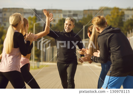 Happy people giving high five to mature man rejoicing the success in sport training outdoors. 130978115