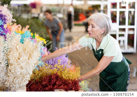Elderly woman, hostess of the flower market, collects Ruscus Italie in bouquet 130978154