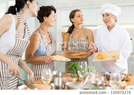 Elderly woman chef teaches group of people how to cook chicken 130978278