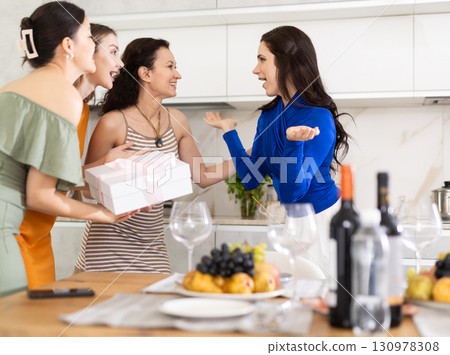 Excited woman greeting besties bringing gift for house party 130978308