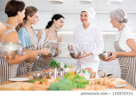 Young lady chef during open culinary lesson tells visitors stages of cooking spicy cream sauce Young lady chef during open culinary lesson tells visitors stages of cooking spicy cream sauce 130978353