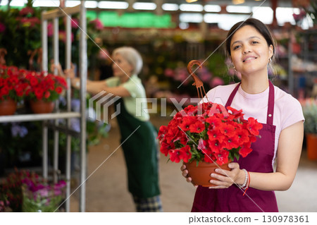Cheerful asian saleswoman offering potted blooming petunias in flower shop 130978361