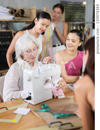 Elderly female teacher shows group how to sew 130978364
