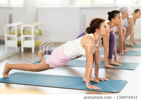 Women practicing in yoga class, focusing on flexibility and relaxation in calm studio setting 130978432