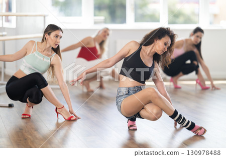 Woman with female perform dance in heels, squat down, actively repeat movements of instructor. 130978488