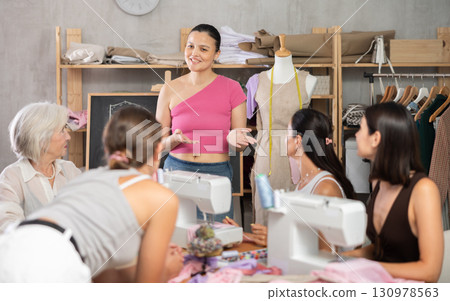 Middle-aged Asian female teacher speaking students during dressmaking class 130978563