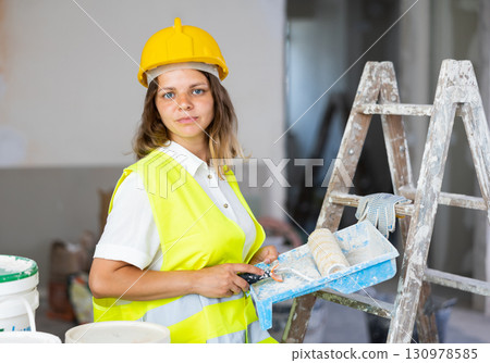 Woman builder holding paint roller and tray, home improvement works 130978585