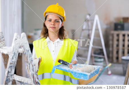 Woman house painter in yellow vest and hardhat in room being renovated Woman house painter in yellow vest and hardhat in room being renovated 130978587