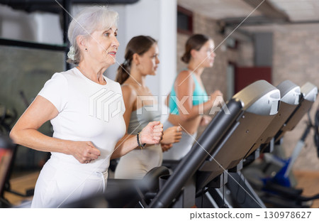 Mature woman running on treadmill in modern fitness club 130978627