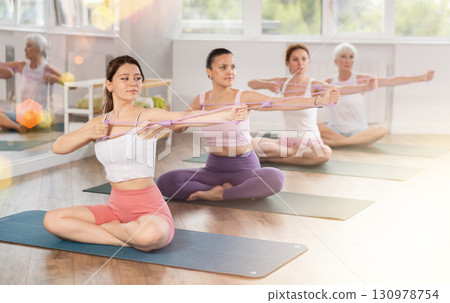 Girl exercising with figure eight resistance band during group pilates class Girl exercising with figure eight resistance band during group pilates class 130978754
