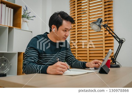 man learning online with tablet and wireless earbuds at home office man learning online with tablet and wireless earbuds at home office 130978866