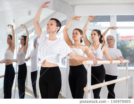 Woman maintaining third position at ballet barre at group rehearsal 130978905