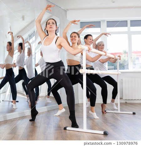 Sporty woman performing wide squats at barre during group training 130978976