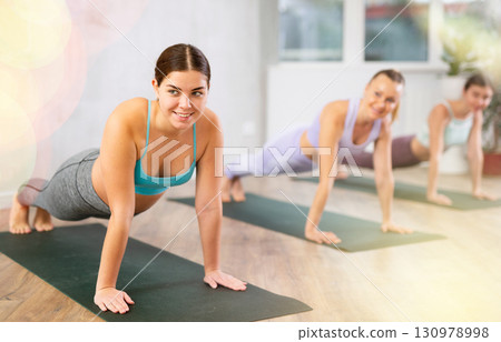 Diligent women practicing plank pose of yoga in light fitness room 130978998