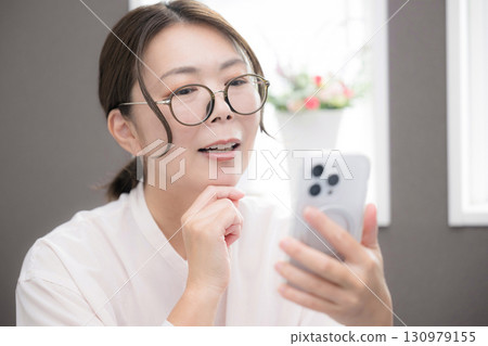Close-up of a smiling woman in her 40s thinking with glasses looking at her smartphone Close-up of a smiling woman in her 40s thinking with glasses looking at her smartphone 130979155