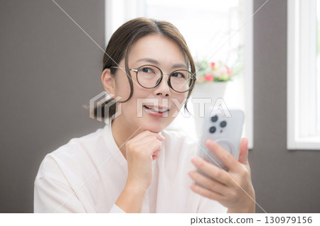 Close-up of a smiling woman in her 40s thinking with glasses looking at her smartphone Close-up of a smiling woman in her 40s thinking with glasses looking at her smartphone 130979156