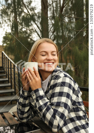 Smiling woman enjoys a warm drink outdoors Smiling woman enjoys a warm drink outdoors 130979219