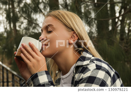 Young woman savoring a cup of coffee surrounded by nature 130979221