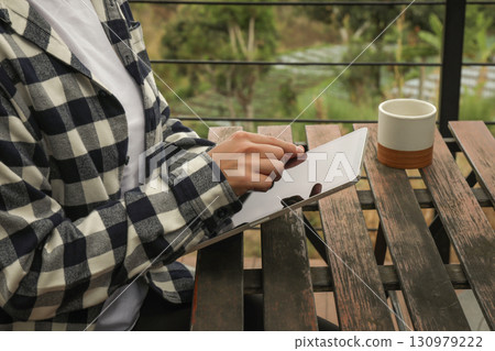 Individual interacts with a tablet while enjoying coffee 130979222