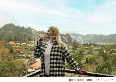 Woman with coffee relaxes on a balcony surrounded by hills 130979226