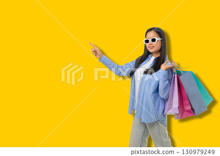 Young woman points while holding shopping bags during sales Young woman points while holding shopping bags during sales 130979249