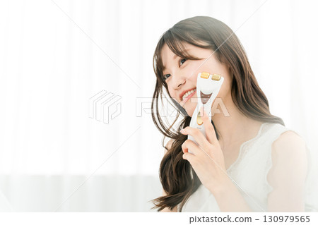 Young Asian woman massaging with a facial beauty device (skin care, lift up) 130979565