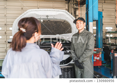 一名男性機械師在修理店向一名女司機解釋汽車 一名男性機械師在修理店向一名女司機解釋汽車 130980956