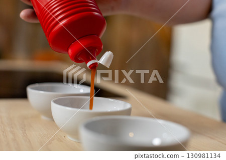 Ketchup Being Poured Generously into Various Dishes for Tasting, Dipping, or Enjoying 130981134