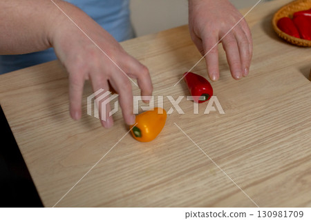 A Vibrant Arrangement of Colorful Peppers Displayed on a Wooden Surface with Hands Involved A Vibrant Arrangement of Colorful Peppers Displayed on a Wooden Surface with Hands Involved 130981709