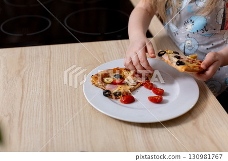 A Happy Child Is Delightfully Enjoying Tasty Pizza with Fresh Ingredients in a Bright Kitchen A Happy Child Is Delightfully Enjoying Tasty Pizza with Fresh Ingredients in a Bright Kitchen 130981767