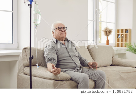Senior man sitting on couch at home while receiving IV drip infusion and vitamin therapy Senior man sitting on couch at home while receiving IV drip infusion and vitamin therapy 130981792