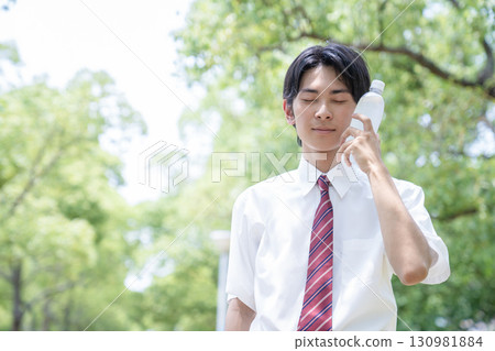 A high school boy holding a plastic bottle to his cheek 130981884