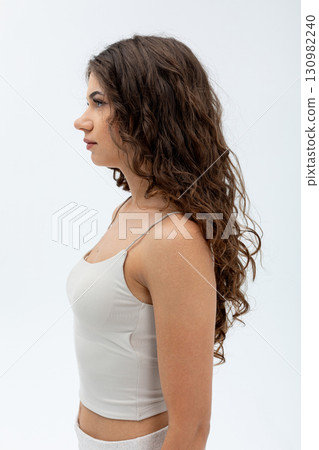 Here is a portrait profile of a beautiful woman showcasing her long, curly hair gracefully 130982240