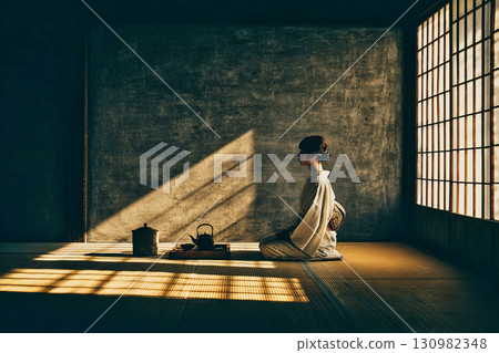 A woman in a kimono sitting upright in a Japanese-style room and performing a tea ceremony 130982348