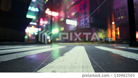 A vibrant street view features neon lights illuminating a wet urban landscape at night. The ground shows striped crosswalks, while colorful lights create a lively atmosphere. 130982503