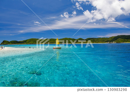 Tourists are landing on the white sand beach of Kabi Island. A beautiful coral reef with parasols, boats, and sabani boats moored. Tourists are landing on the white sand beach of Kabi Island. A beautiful coral reef with parasols, boats, and sabani boats moored. 130983298