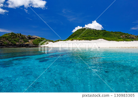 Tourists are landing on the white sand beach of Kabi Island. A beautiful coral reef with parasols, boats, and sabani boats moored. Tourists are landing on the white sand beach of Kabi Island. A beautiful coral reef with parasols, boats, and sabani boats moored. 130983305