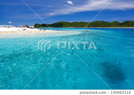 Tourists are landing on the white sand beach of Kabi Island. A beautiful coral reef with parasols, boats, and sabani boats moored. 130983310