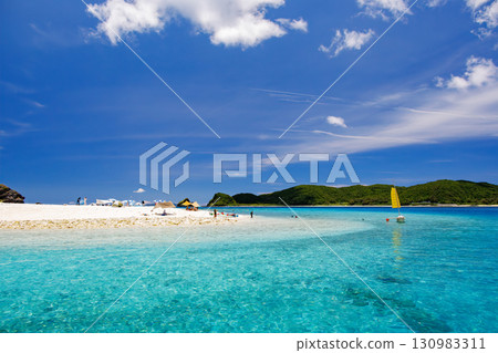 遊客登上卡比島的白色沙灘。美麗的珊瑚礁，停泊著遮陽傘、船和鰹魚船。 130983311