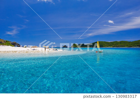 Tourists are landing on the white sand beach of Kabi Island. A beautiful coral reef with parasols, boats, and sabani boats moored. 130983317