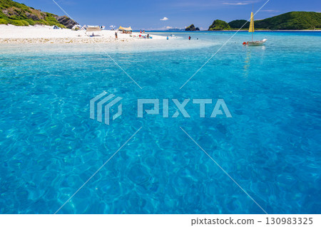 Tourists are landing on the white sand beach of Kabi Island. A beautiful coral reef with parasols, boats, and sabani boats moored. 130983325