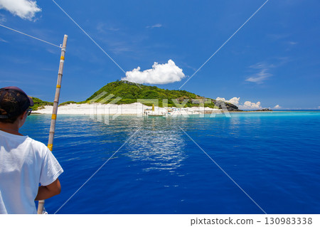 遊客登上卡比島的白色沙灘。美麗的珊瑚礁，停泊著遮陽傘、船和鰹魚船。 130983338